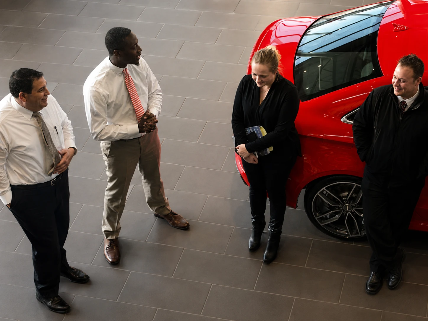 Professional showroom discussion beside a red vehicle